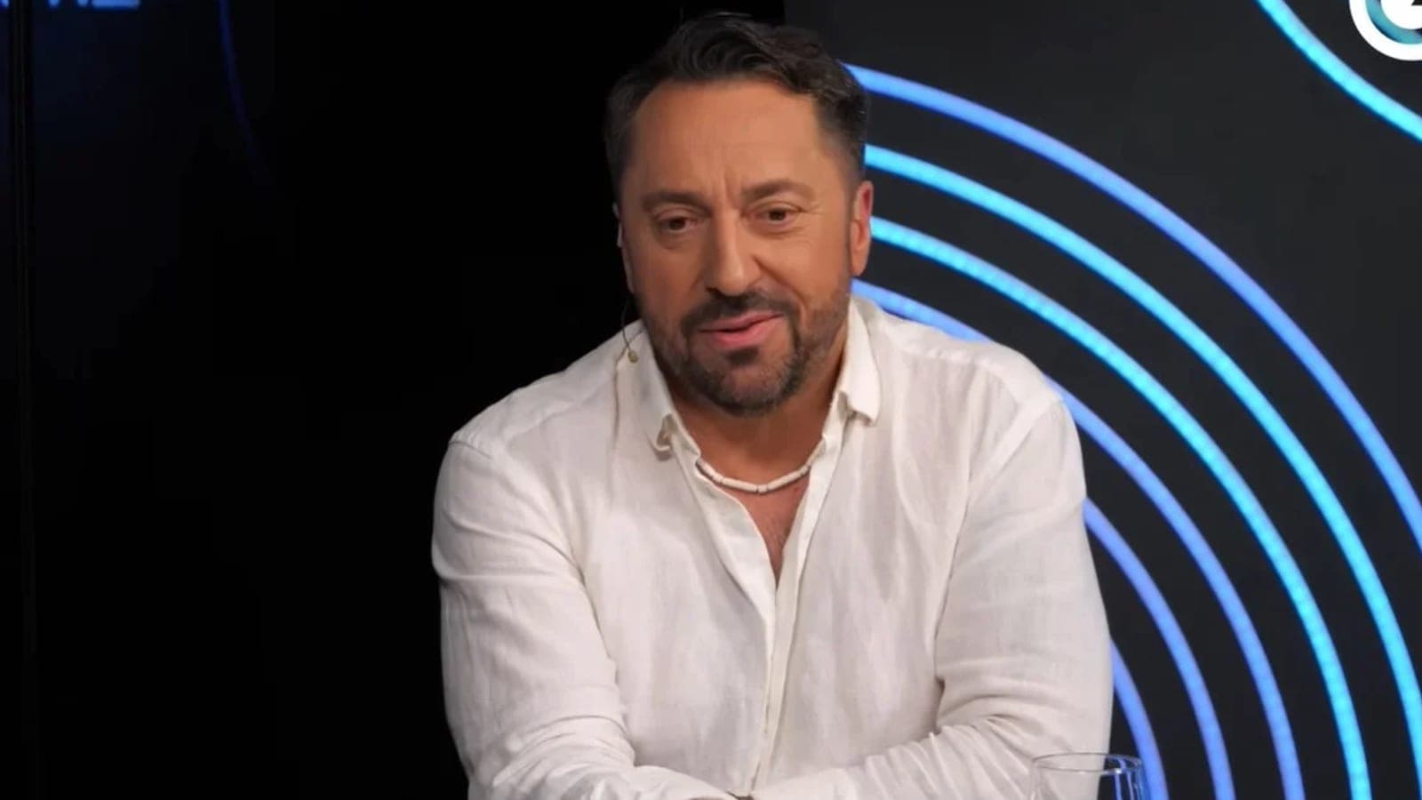 Marcin Miller w białej lnianej koszuli podczas nagrania w studiu, na tle ciemnej ścianki z niebieskimi neonami